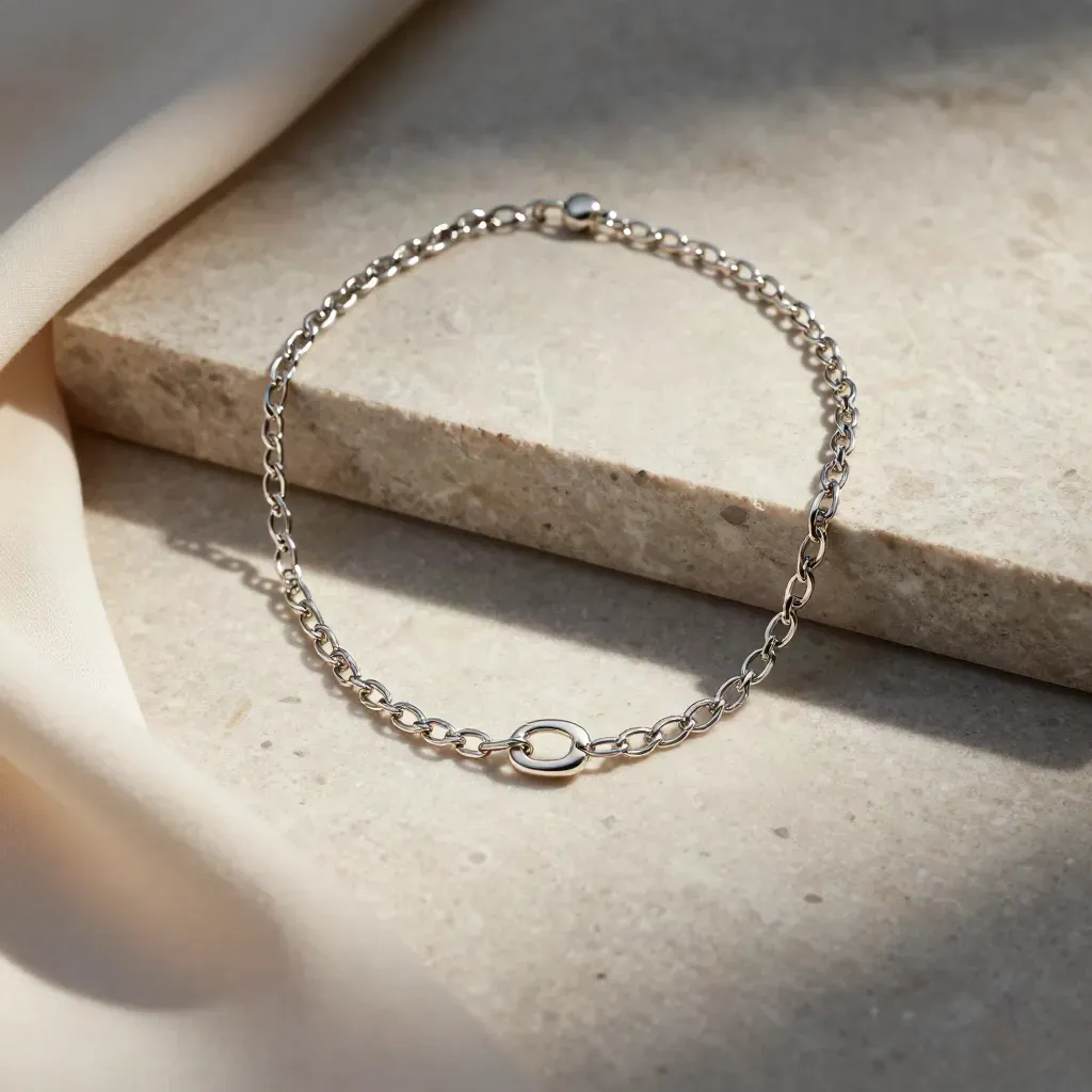 Silver link necklace on a pale stone arc with folded cloth and soft luminous haze.